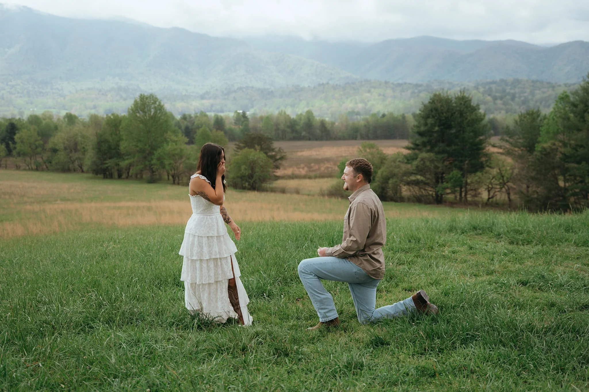 Surprise proposal in Cades Cove meadow with man kneeling as woman reacts in the Great Smoky Mountains