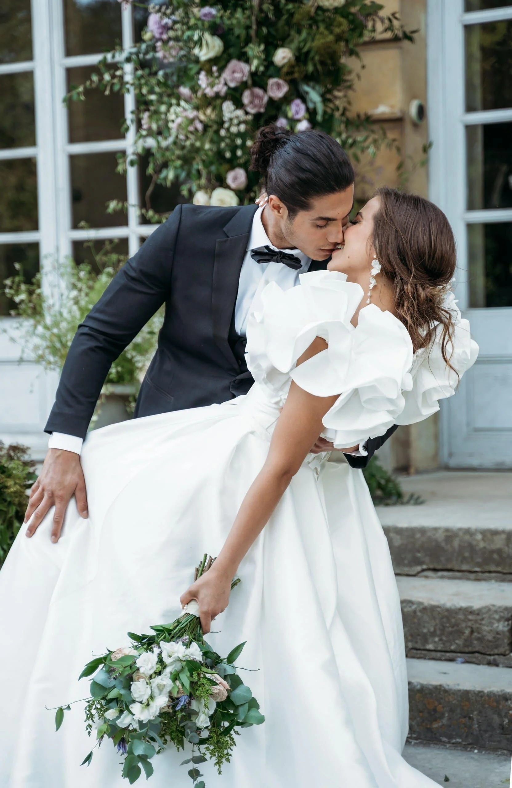 IMG_8973 Bride and groom sharing a romantic dip kiss outside an elegant European-style venue during their wedding day